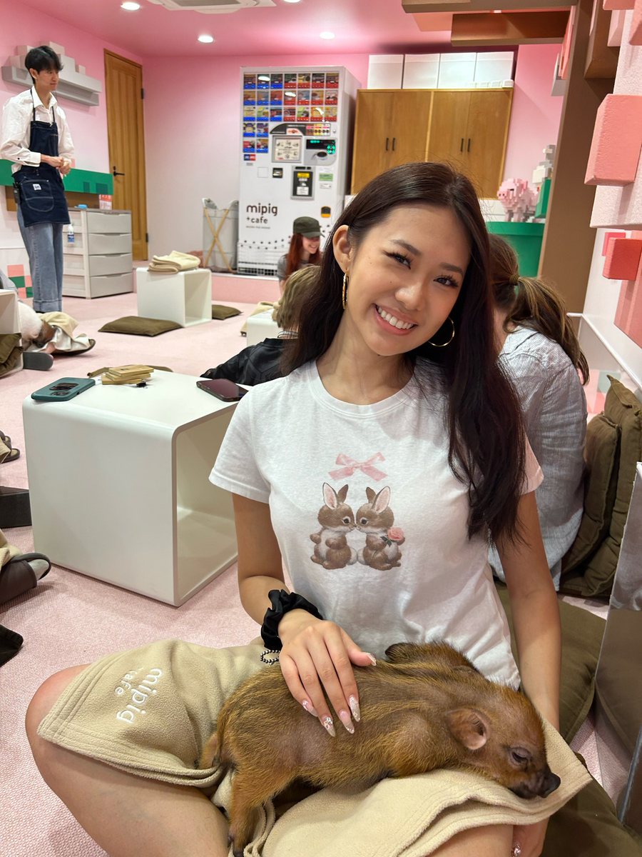 Angela smiling with a mini pig on her lap at a mini pig café in Japan
